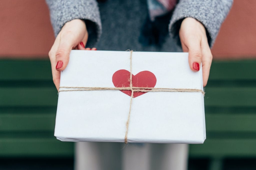 Top view of a gift in paper packaging decorated with a heart in female hands outside