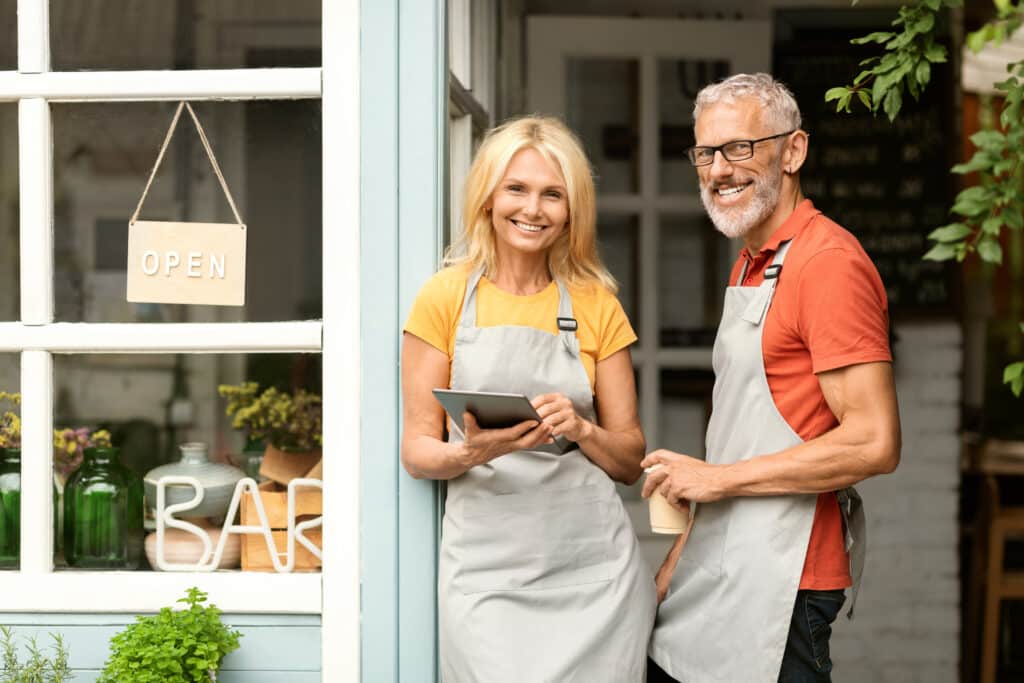Two smiling business owners standing at the door of their shop
