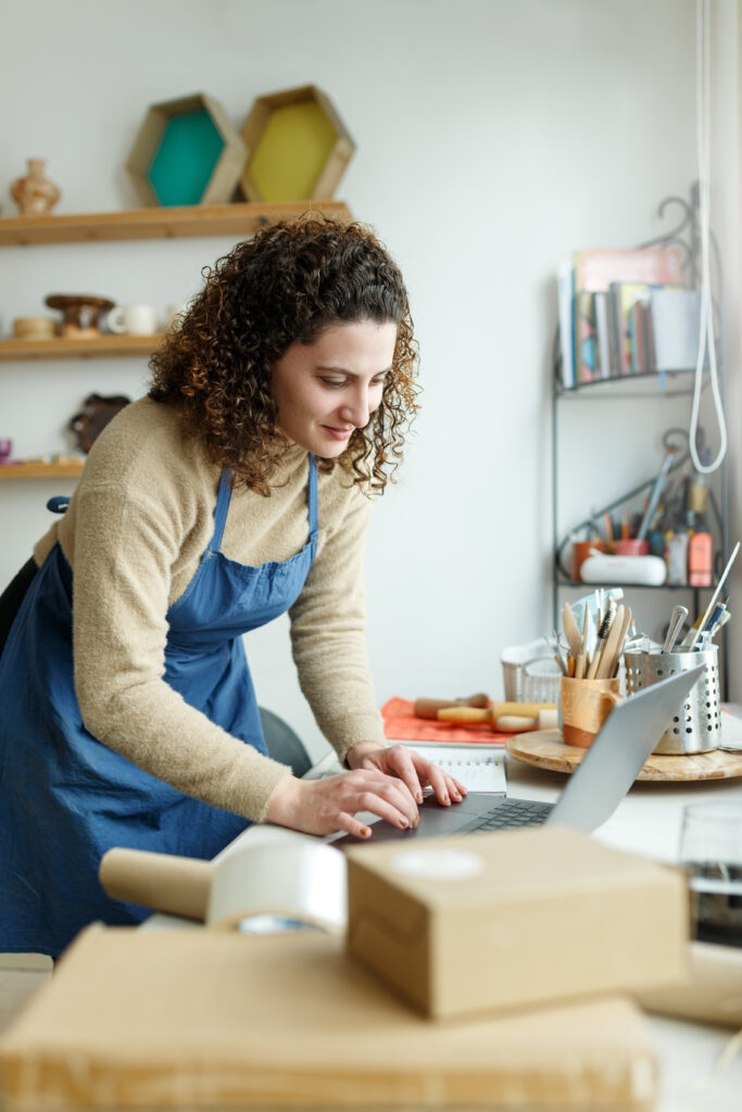 Small business owner in an apron working on a laptop in her workshop