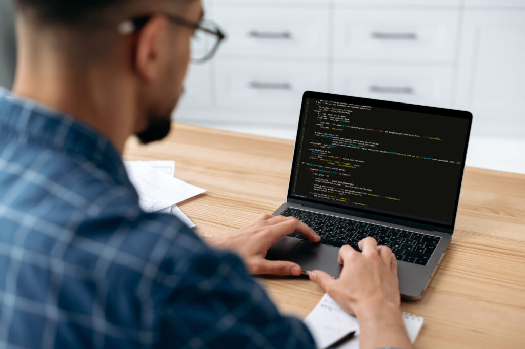 Developer working on code at a laptop on a light wood desk