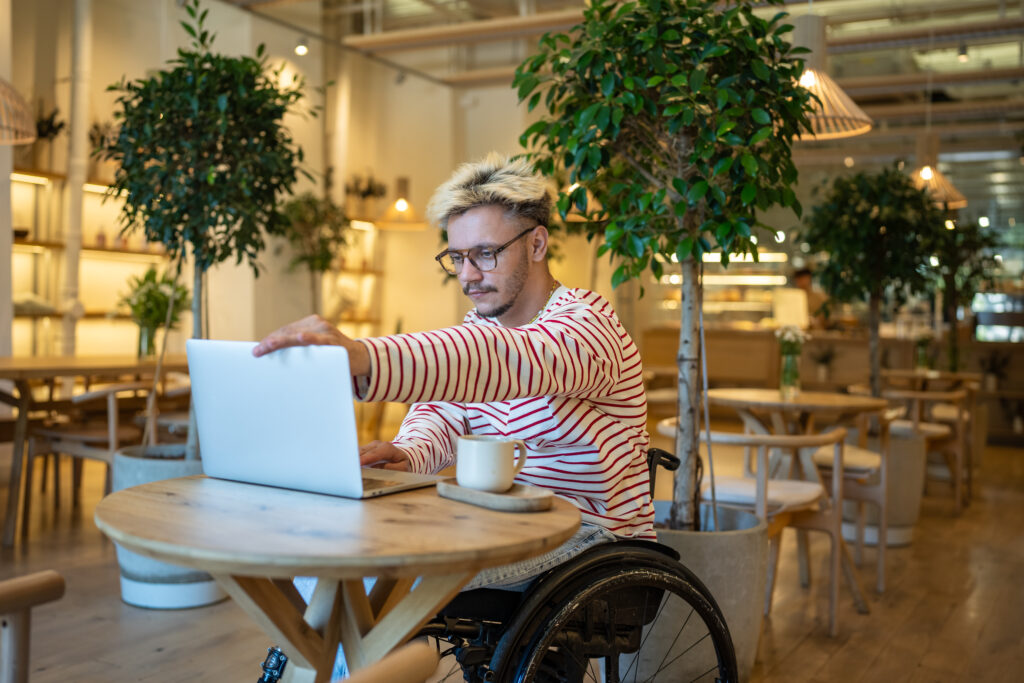 Man in a wheelchair using a laptop at a table in an airy cafe