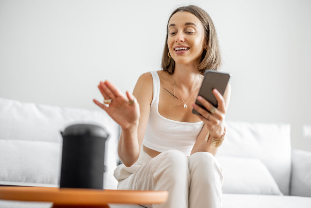 Woman asking a smart speaker a question while holding her phone at home