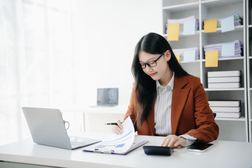 Woman typing on a tablet and laptop at a wooden desk